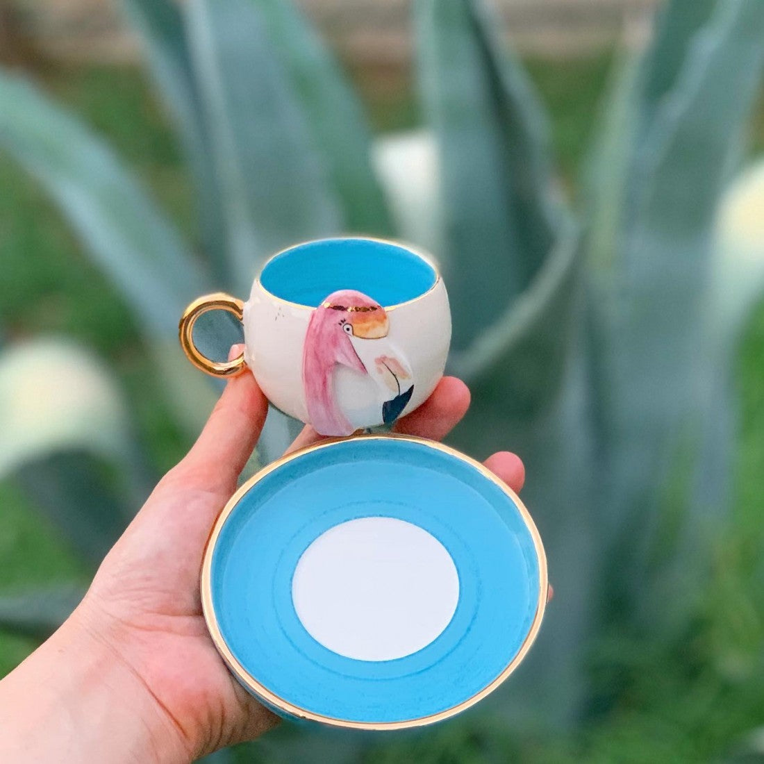 Blue ceramic flamingo coffee cup and saucer with gold rim, pink bird on white