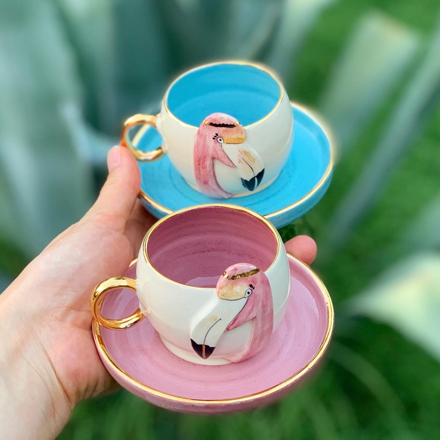 Set of flamingo coffee cups: blue and pink cups with gold handles on saucers